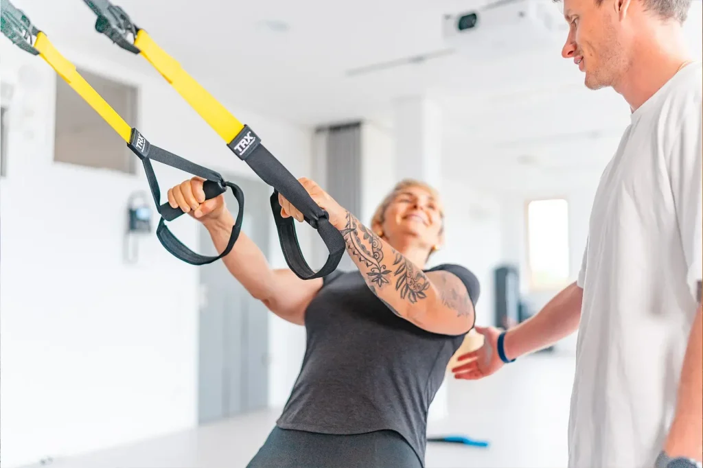 Eine Person führt ein TRX-Training unter Anleitung eines Trainers durch.