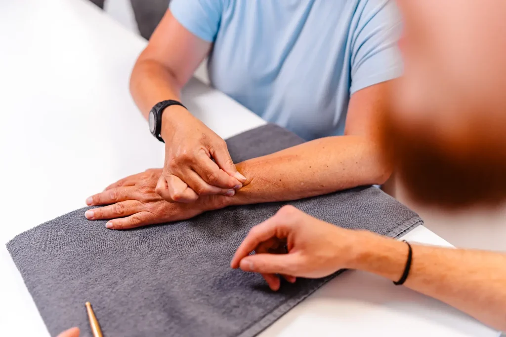 Eine Ergotherapie-Sitzung im Therapie Zentrum Augsburg: Therapeut arbeitet präzise an der Hand eines Patienten auf einer grauen Unterlage.