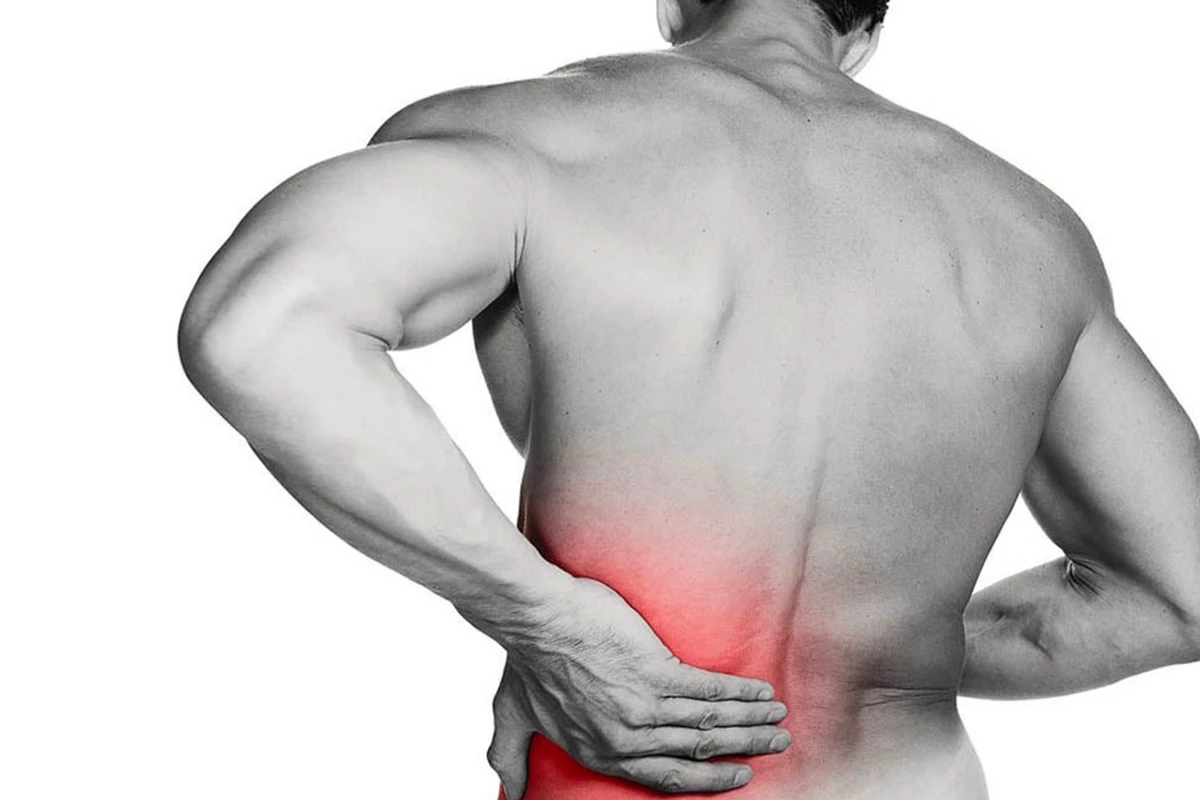 Muskelbepackter Mann greift sich mit schmerzverzerrtem Gesicht an den unteren Rücken – Darstellung typischer Rückenschmerzen, wie sie im Therapie Zentrum behandelt werden.