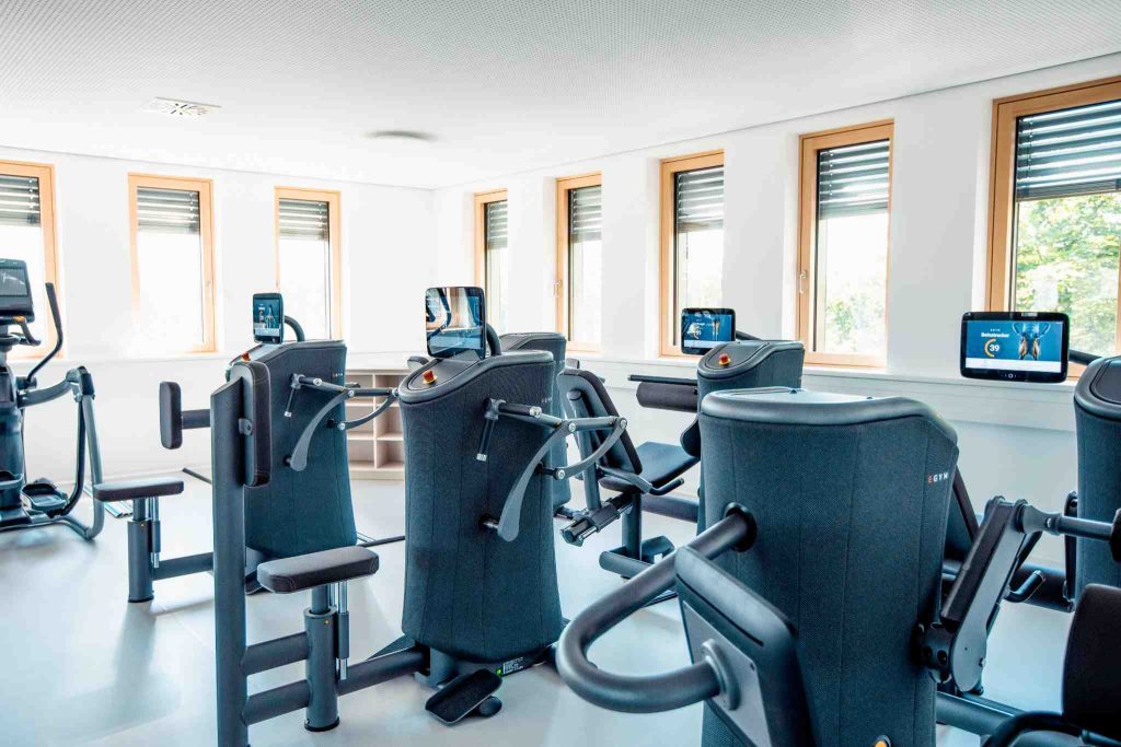 „Moderner Trainingsraum mit vernetzten Trainingsgeräten in einer Physiotherapie Praxis, helle Umgebung mit mehreren Geräten zur therapeutischen Bewegungstherapie