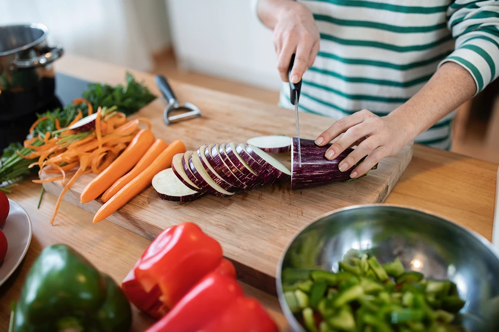 Frisches Gemüse wird in der Küche geschnitten (Karotten, Aubergine, Paprika, Kräuter) – nährstoffreiche Ernährung zur Unterstützung der Telomere und für gesundes biologisches Altern
